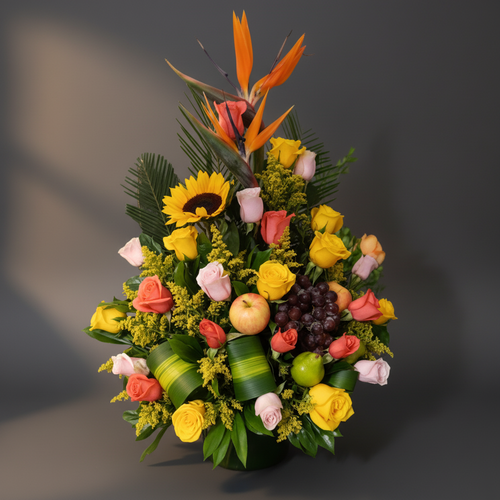 Arreglo floral vertical con rosas de colores, girasol, aves del paraíso y frutas como uvas, manzana y limón sobre fondo gris
