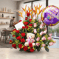 Arreglo floral de rosas rojas y rosas con aves del paraíso, globo de feliz cumpleaños y oso de peluche sobre mesa en sala comedor moderna con hombre al fondo preparando la mesa