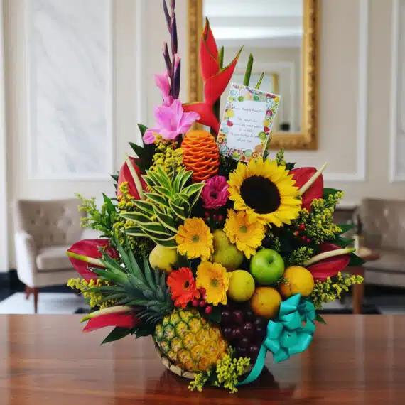 Arreglo Floral Exótico Antídoto con Frutas Frescas y Flores Vibrantes Arreglo floral exótico Antídoto con girasoles, heliconias, gladiolos, piña, uvas, peras y manzanas sobre mesa de madera pulid