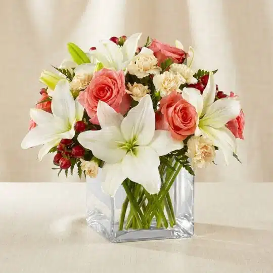 Arreglo floral Fabrizia con rosas rosadas, lirios blancos, claveles crema y bayas rojas en un jarrón de cristal cuadrado, ide