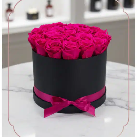 Arreglo Floral Marena con 21 rosas fucsia vibrantes y frescas en una caja redonda negra con lazo fucsia, sobre una mesa de má