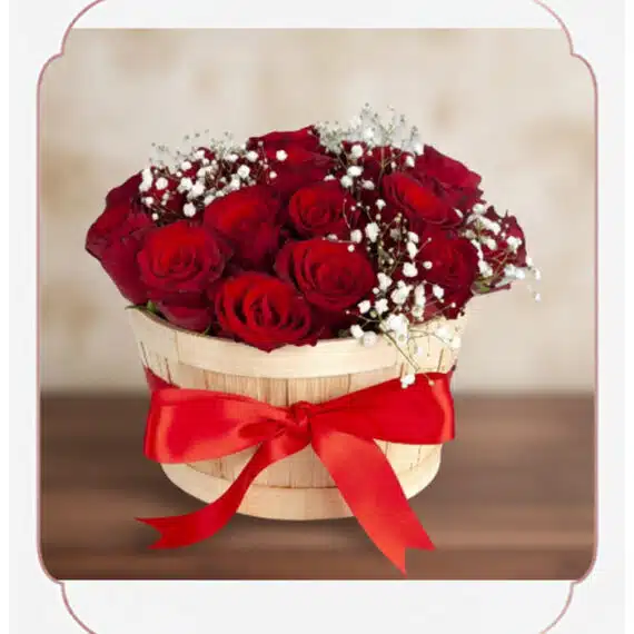 Arreglo Lidia: 15 Rosas Rojas Premium en Balde Rústico Elegante Arreglo floral 'Lidia' con 15 rosas rojas premium en un balde rústico de madera, adornado con un lazo rojo y follaje blanco,