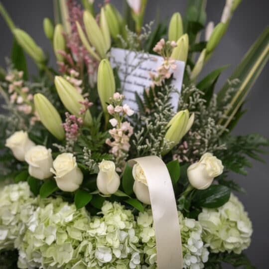 Fotografía macro premium de arreglo fúnebre 'Eterno Descanso' con lirios, rosas blancas y hortensias verdes, rocío sutil, cin