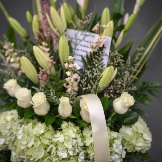 Fotografía macro premium de arreglo fúnebre 'Eterno Descanso' con lirios, rosas blancas y hortensias verdes, rocío sutil, cin