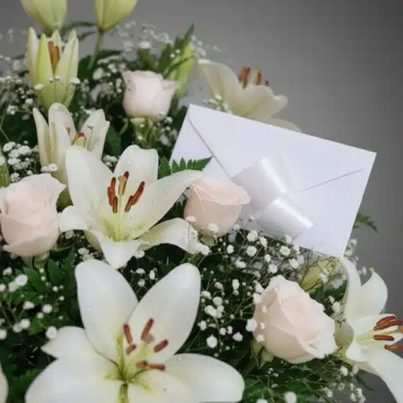 Fotografía macro premium del Arreglo Fúnebre Infinito con lirios blancos, rosas pálidas y follaje verde, con rocío sutil y ci