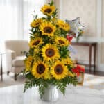 Arreglo floral premium con girasoles vibrantes y follaje verde, presentado en un jarrón blanco sobre una mesa de mármol en un