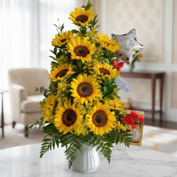 Arreglo floral premium con girasoles vibrantes y follaje verde, presentado en un jarrón blanco sobre una mesa de mármol en un