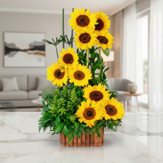 Arreglo con Girasoles Verano sobre Mármol: Frescura y Elegancia Floral Arreglo floral con girasoles vibrantes y follaje verde en una base de madera, sobre una superficie de mármol pulido en un ent