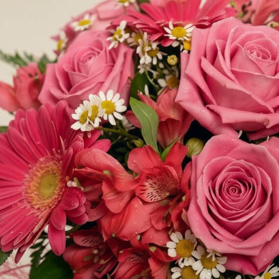 Primer plano extremo del Bouquet ORLENA con rosas rosadas, gerberas fucsia, alstroemerias rojas y margaritas blancas, con got