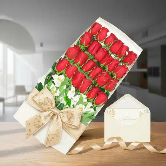 Caja de 24 rosas rojas frescas con alstroemerias blancas, lazo dorado y tarjeta de regalo en un sobre, sobre una mesa de made