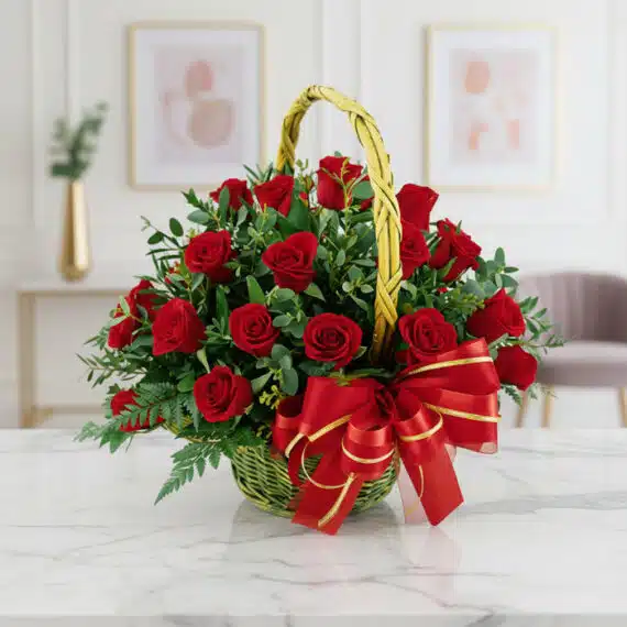 Canasta Floral Premium con 24 Rosas Rojas Frescas y Elegantes Canasta floral de mimbre verde con 24 rosas rojas vibrantes, follaje verde y un lazo rojo brillante, sobre una mesa de mármol