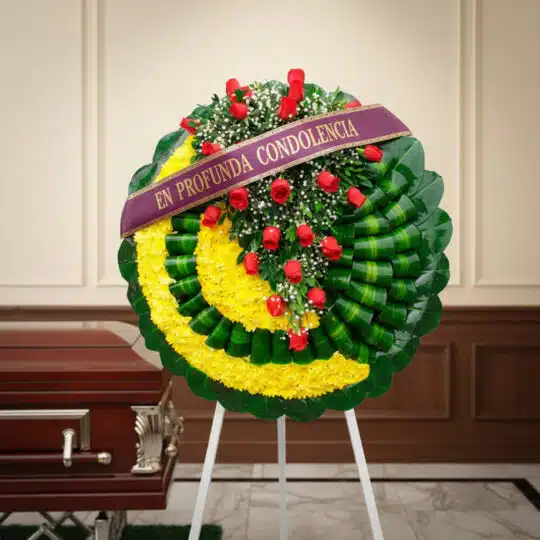 Corona fúnebre Adela con rosas rojas y flores amarillas, cinta morada 'En Profunda Condolencia', junto a un ataúd en sala de