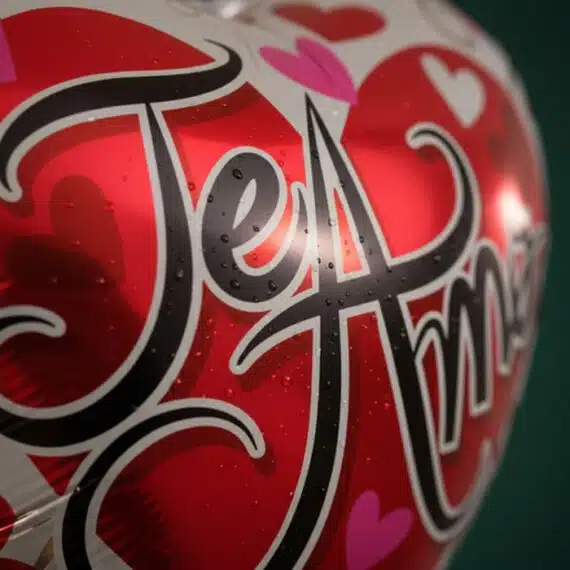 Primer plano extremo de un globo metalizado rojo y blanco con la frase 'Te Amo' en negro, cubierto de sutiles gotas de rocío