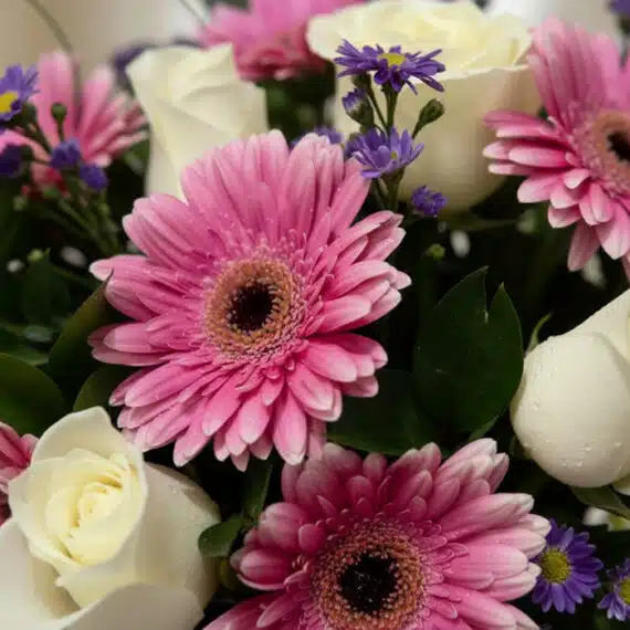 Primer plano extremo de un arreglo floral 'Jarrón Primavera' con gerberas rosas, rosas blancas y pequeñas flores moradas, tod