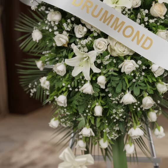 Pedestal conmemorativo Legado de Marcos con arreglo floral fúnebre en tonos blancos y cremas, rosas, lirios y follaje verde,