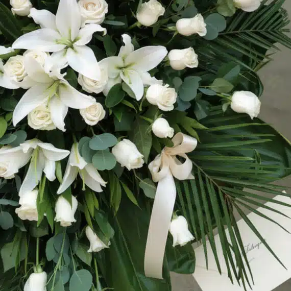 Fotografía macro premium del Pedestal Fúnebre Eternidad, mostrando lirios blancos, rosas crema y follaje verde con rocío suti