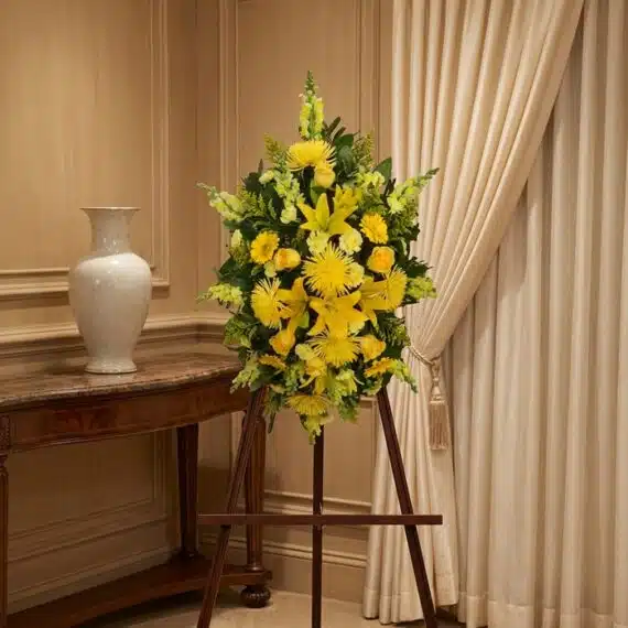Pedestal de homenaje "El Legado de Sebastian" con un arreglo floral fúnebre de lirios y crisantemos amarillos, presentado ele